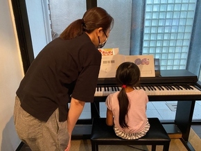 「<楽しい>の達人」が子どもにピアノを教えている写真